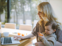 Woman-holding-baby-uses-laptop