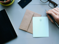 desk-with-notebook-letter-envelope-pen-hand-viewed-from-above