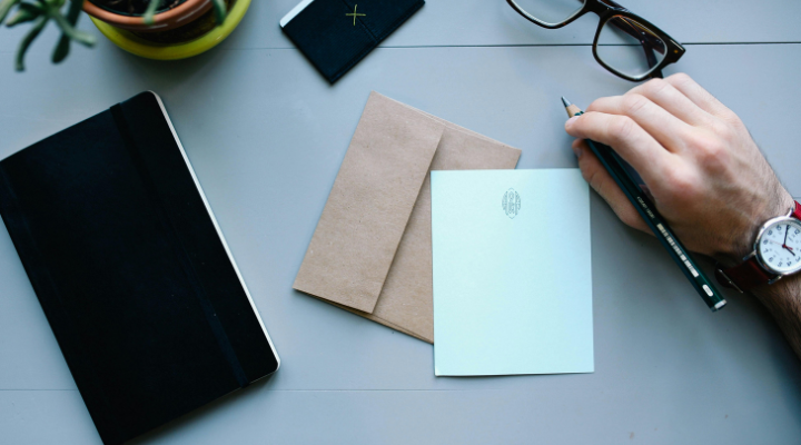 desk-with-notebook-letter-envelope-pen-hand-viewed-from-above