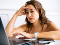 frowning-woman-with-hand-to-forehead-sitting-in-front-of-laptop