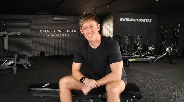 Man in black gym clothes sitting in dark gym with fitness machines in the background