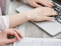 Close-up of hands on desk with application form and laptop.