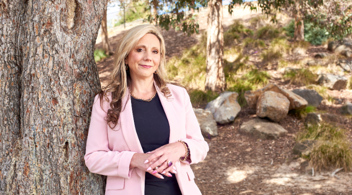 businesswoman-wearing-pink-blazer-leaning-against-tree