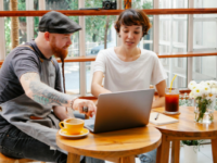 A woman and a man in an apron work on a laptop at a cafe table.