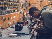 Man in metalwork studio leaning over bench using tool.