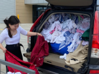 A woman unloading donated clothing from the back of a car.