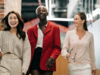 Three smiling women wearing business clothes walk down corridor