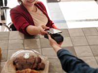 A woman in a wheelchair at a cafe counter paying using a smartphone.