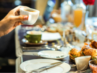 Closeup of a businessman's hand holding a cup over a dining table.