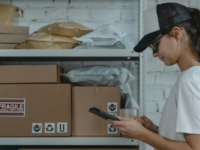 Woman on phone standing by shelf of parcels.