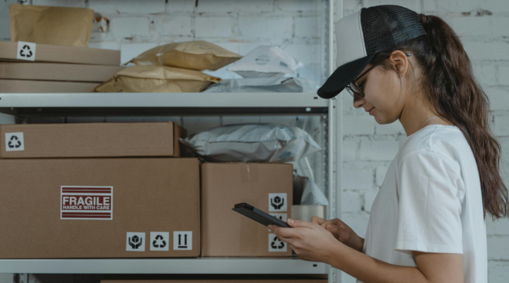 Woman on phone standing by shelf of parcels.